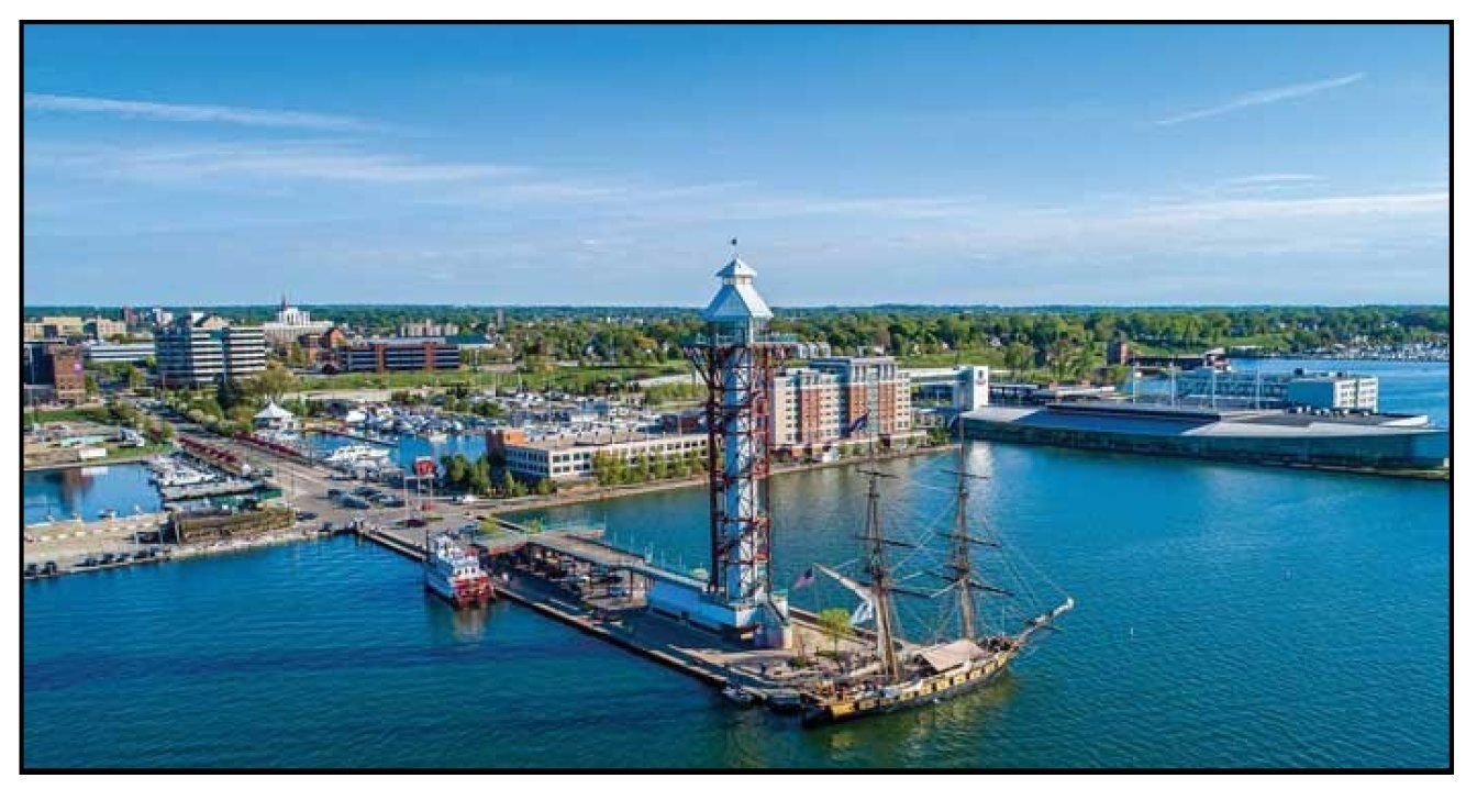 Aerial view of the Erie, Pennsylvania bayfront, showing the Bicentennial Tower, the U.S. Brig Niagara tall ship, the Bayfront Convention Center, and the downtown Erie skyline on a clear summer day